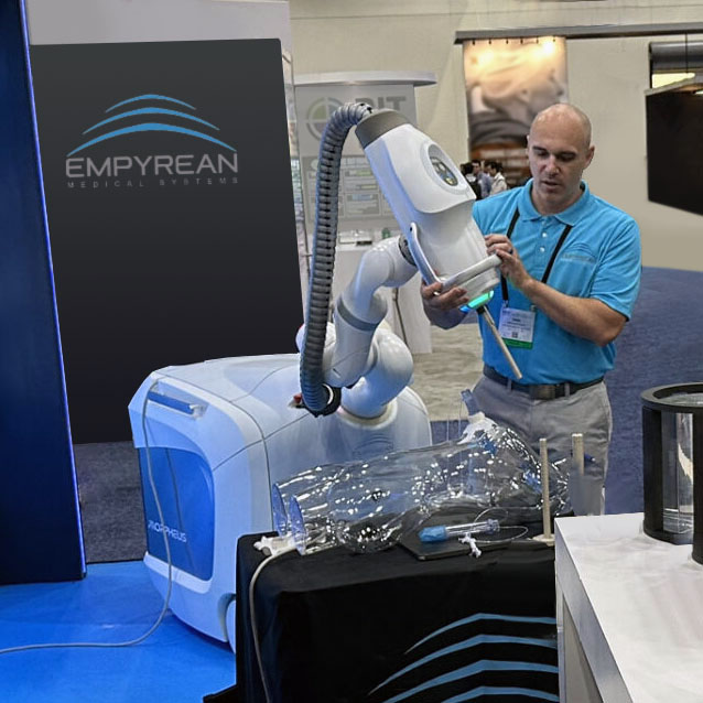 A man demonstrates the Empyrean Morpheus medical robotic system at a trade show booth.
