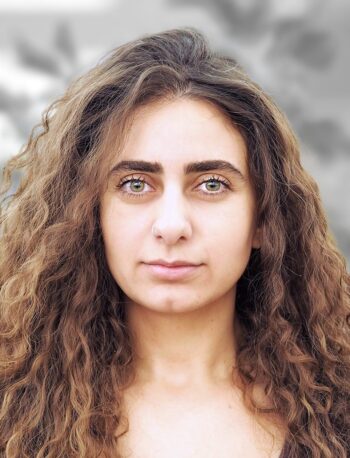 A portrait of Lilit Karayan, a woman with long curly hair and green eyes is looking directly at the camera with a neutral expression. The background is blurred.